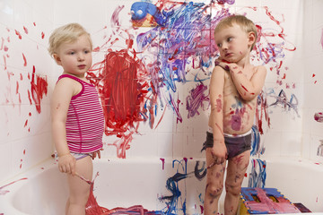 Naklejka premium Portrait of two cute adorable white Caucasian little boy and girl playing painting on walls in bathroom, having fun, lifestyle active childhood concept, early education development