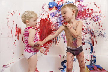 Naklejka premium Portrait of two cute adorable white Caucasian little boy and girl playing painting on walls in bathroom, having fun, lifestyle active childhood concept, early education development