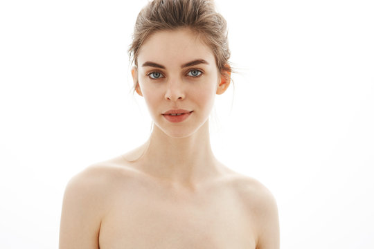 Portrait of young beautiful tender naked girl with bun looking at camera over white background.