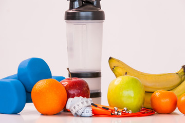 The concept of a healthy diet. Fintes meals. Sport lifestyle. Dumbbells. Shaker. Oranges. Apples. Bananas. fruit juice. The skipping rope. Measuring tape waist. on a white background. studio shooting.