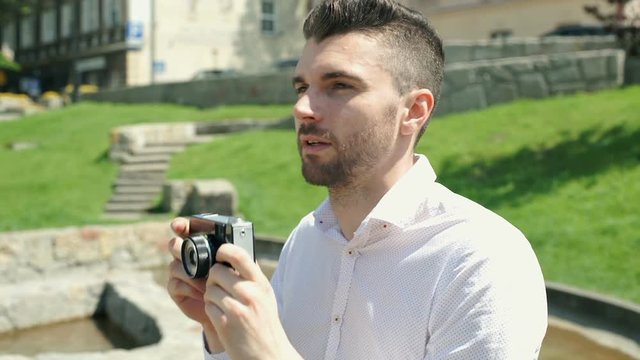 Handsome man doing photos on old camera in the park and enjoying that, steadycam shot
