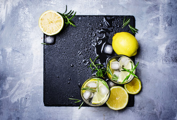 Summer cocktail with lemon, rosemary and ice, gray background, top view