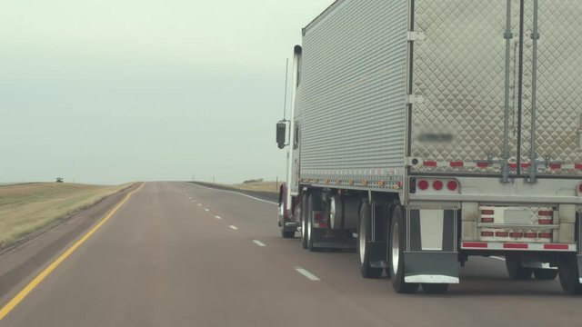 FPV CLOSE UP: Overtaking freight container semi truck driving along the multiple lane highway in US countryside. Freight semi-truck transporting goods, people on road trip traveling in sunny summer