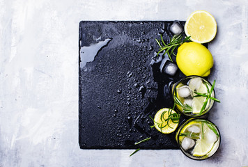 Summer cocktail with lemon, rosemary and ice, gray background, top view