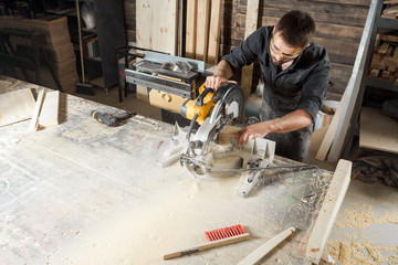 A young male carpenter builder saws a modern circular saw a wooden board in the workshop room © Виталий Сова