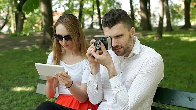 Girl using tablet while her boyfriend doing photos on old camera, steadycam shot
