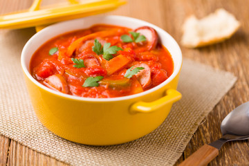 Delicious letcho with fresh vegetables, served in a yellow pot with the fresh bun.