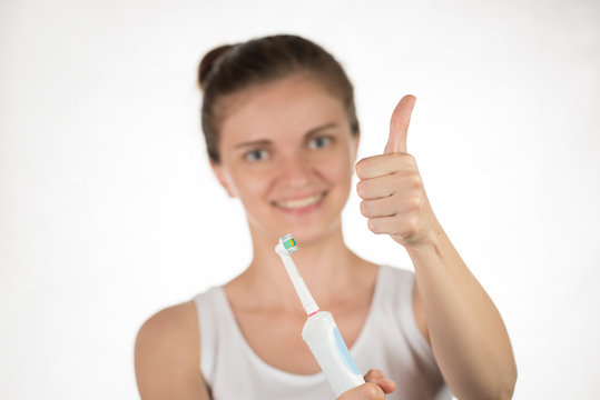 Hygiene of the oral cavity. Young girl with snow-white smile shows okay on a classroom electric toothbrush.