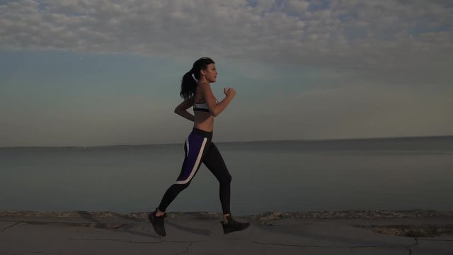 young woman runs lightly along the surf line. The girl is jogging at sunset