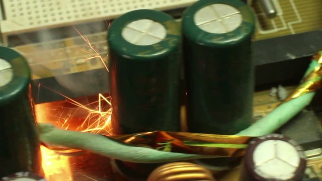Extreme close up of burning and sparking computer components on a motherboard; capacitors and other hardware can be clearly seen . One of a series 