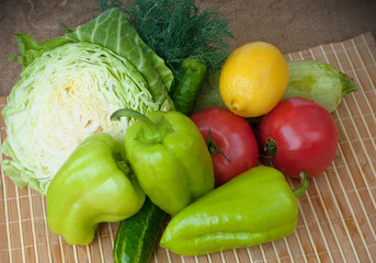 A group of tomatoes, cucumbers, green pepper, zucchini, dill, a half of cabbage and a lemon on the wooden background