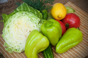 A group of tomatoes, cucumbers, green pepper, zucchini, dill, a half of cabbage and a lemon on the wooden background