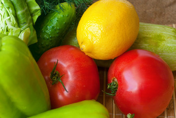 A group of tomatoes, cucumbers, green pepper, zucchini, dill, a half of cabbage and a lemon on the wooden background