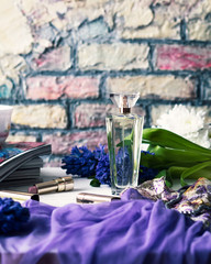glass perfume bottle surrounded by flowers, purple underwear, lipsticks and magazines
