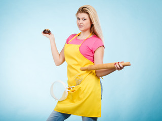 Woman holding cupcake, rolling pin, colander wearing apron