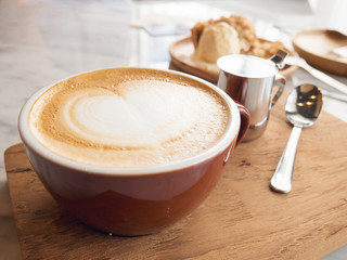 a cup of hot coffee with heart latte art and milk mug and spoon on wood plate with marble table as background
