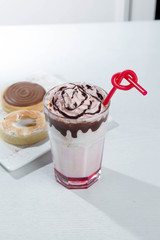 Glass of strawberry milkshake with whipped cocolate cream and fresh strawberries on pink
