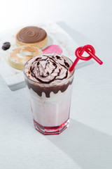 Glass of strawberry milkshake with whipped cocolate cream and fresh strawberries on pink