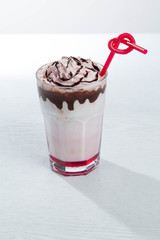 Glass of strawberry milkshake with whipped cocolate cream and fresh strawberries on pink