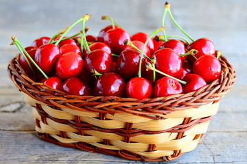 Red sweet cherry in a brown wicker basket and on a vintage wooden table. Summer sweet cherry season concept. Closeup