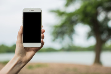 Female holding Smartphone  lake with tree background 