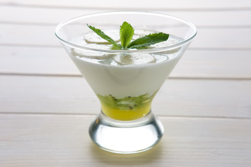 Glass with yogurt with banana and kiwi with honey decorated with mint leaf on top