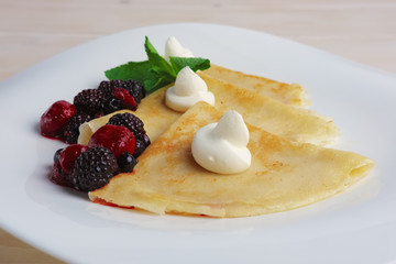 Portion on thin pancakes with sweet cream cheese and berries.