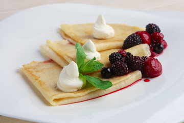Portion on thin pancakes with sweet cream cheese and berries.