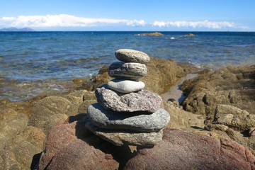 cairn of stacked stones beside sea sunny day