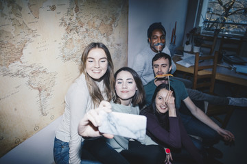 High angle view of cheerful young friends sitting on sofa taking selfie at college dorm