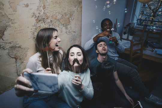 High angle view of young friends sitting on sofa taking selfie at college dorm