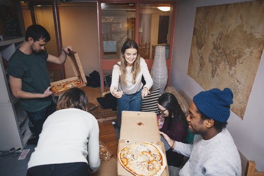 High angle view of young friends enjoying pizza party in dorm room