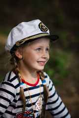 Portrait of a little cheerful girl in the uniform of a sailor and a sea cap. Close.