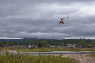 Yellow helicopter comes in to land, an abandoned area around the old village, river, forest....