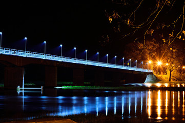 Fototapeta na wymiar Most nad rzeka w nocy oświetlony latarniami.