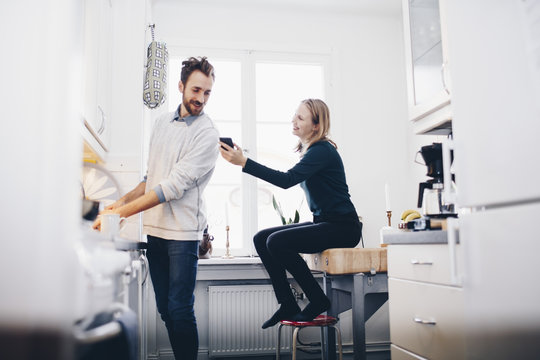 Happy woman showing mobile phone to man in kitchen at home