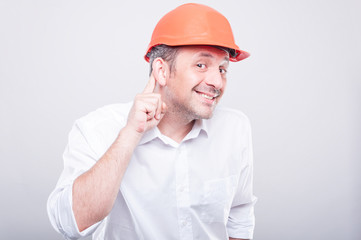 Portrait of contractor wearing hardhat making can't hear gesture
