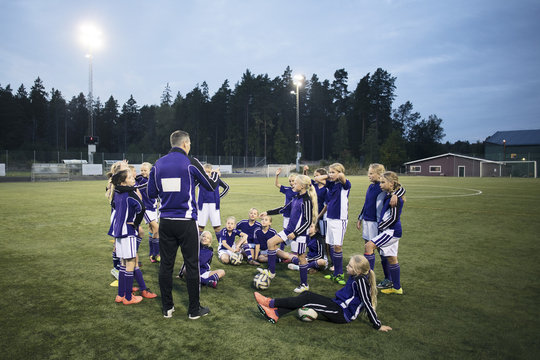 Coach explaining with girls soccer team on field against sky