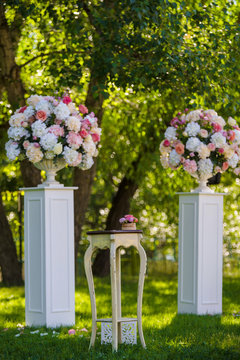 White antique vases with tenderness flowers and vintage table stand on the lawn grass in the garden. Wedding ceremony