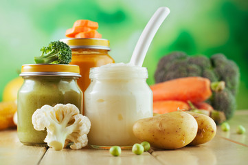 Jars with vegetable puree on the light wooden background