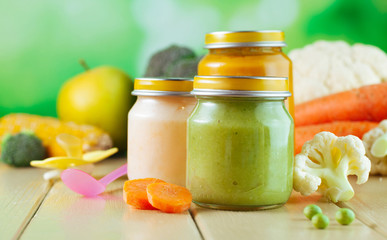 Jars with vegetable puree on the light wooden background