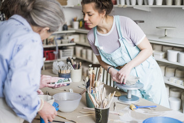 Mature potter showing mobile phone to female colleagues at ceramics workshop