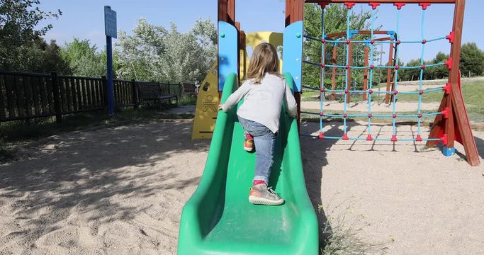 Three years old blonde child playing trying to climb on green plastic small slide and falling. Outdoor playground, in public Park Valdebebas, Madrid Spain
