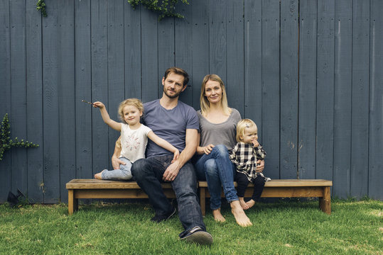 Portrait of happy parents and children sitting on seats against fence at yard