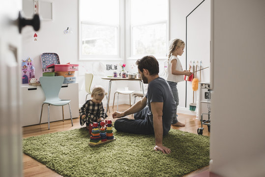 Father and daughters playing with toys in playroom at home