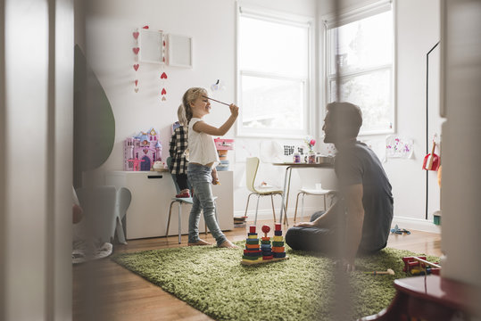 Father looking at daughters playing with toy in playroom at home