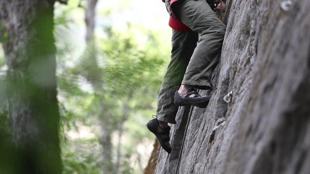 Rock climbing detail of climber shoes and legs on straight vertical wall. . Slow motion 120fps detail close up. Extreme risk outdoor sport. Woods and trees on the background. Patagonia Argentina