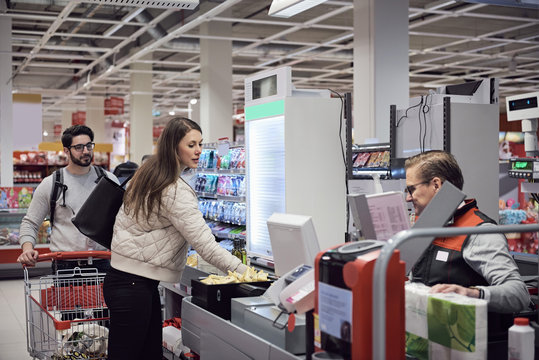 Man looking at woman paying to mature cashier in supermarket