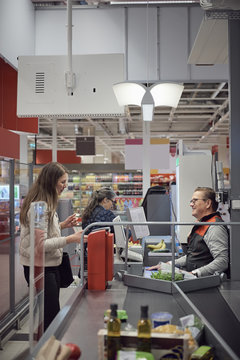 Woman talking to mature cashier while paying at checkout counter in supermarket