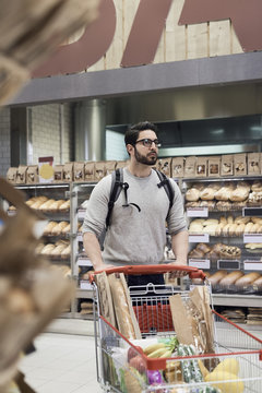 Man pushing shopping cart with groceries against rack at supermarket